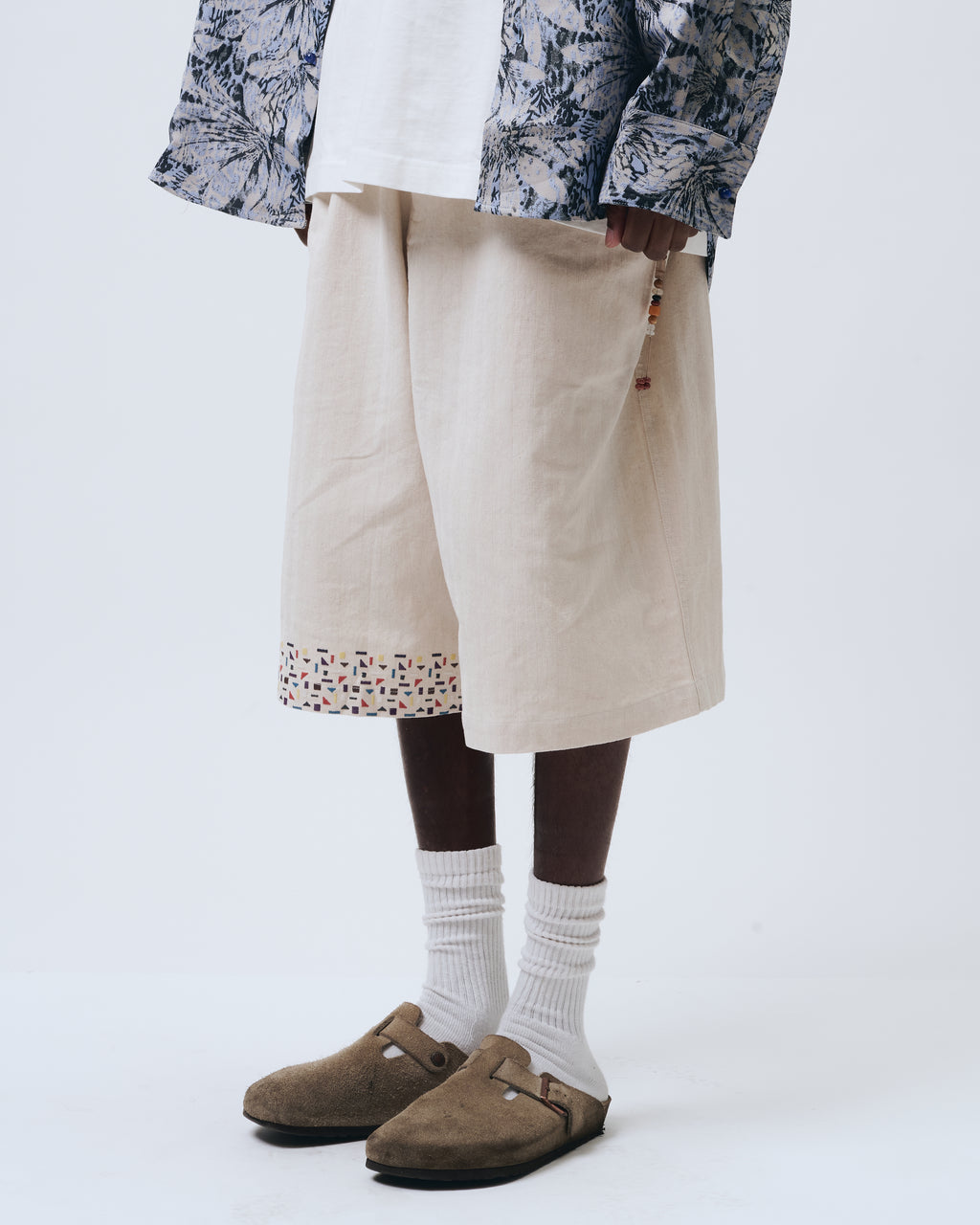 Person wearing a patterned jacket, beige pants, white socks, and brown shoes on a white background