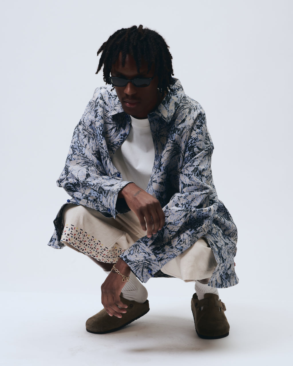 Person wearing a patterned jacket and sunglasses on a white background