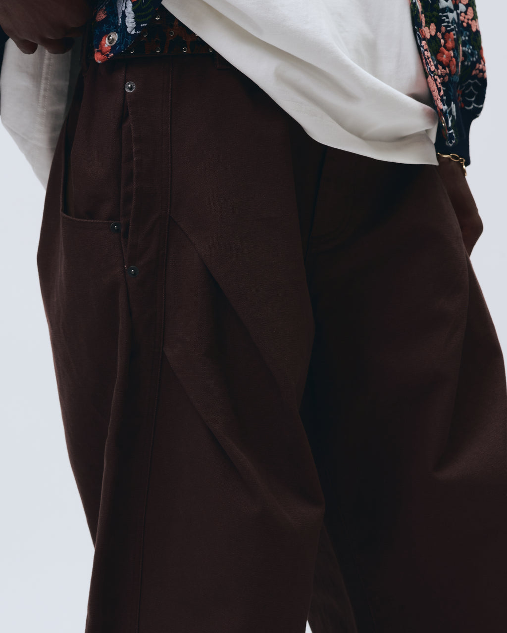 Brown pants worn with a white shirt and floral jacket on a light gray background
