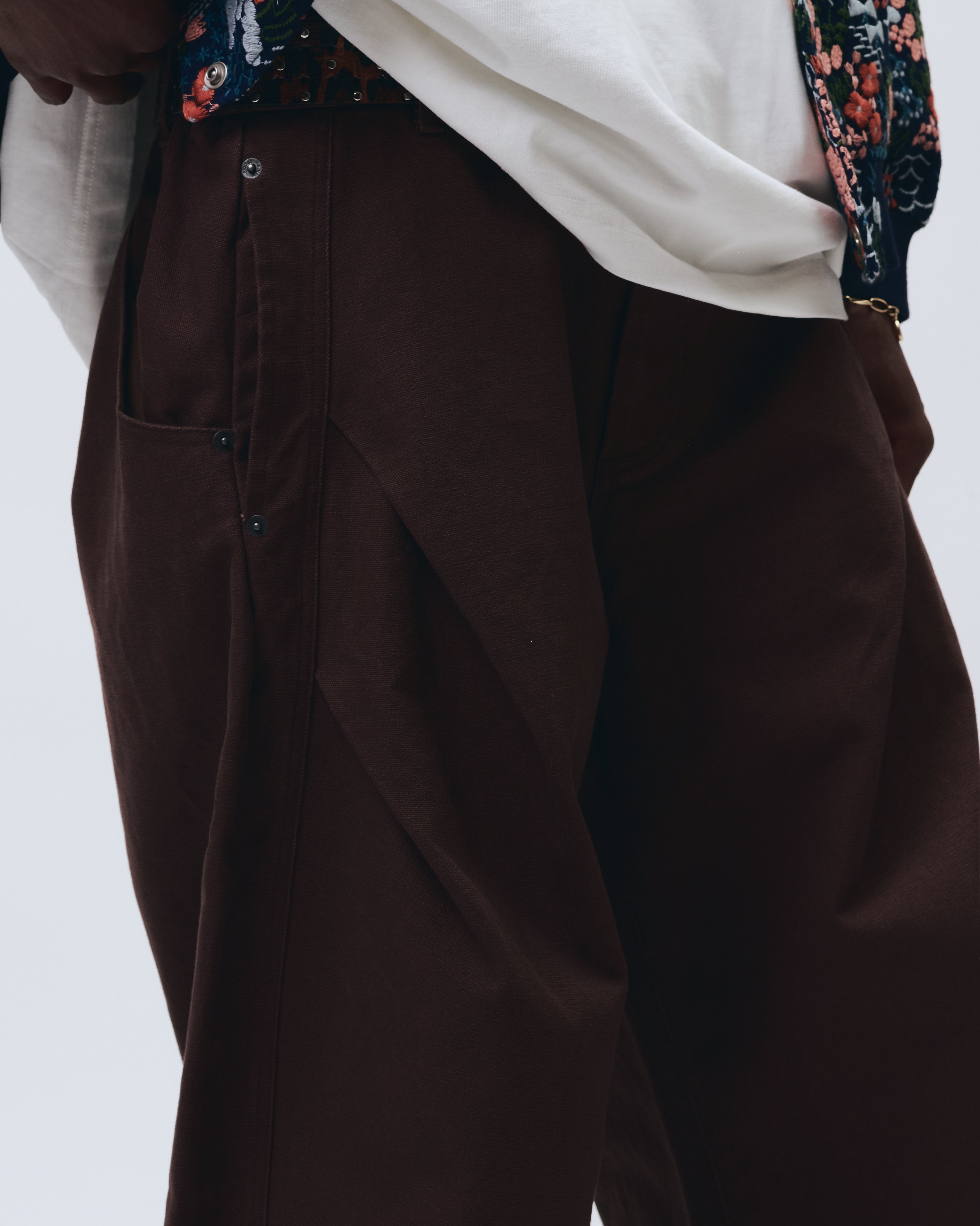 Brown pants worn with a white shirt and floral jacket on a light gray background