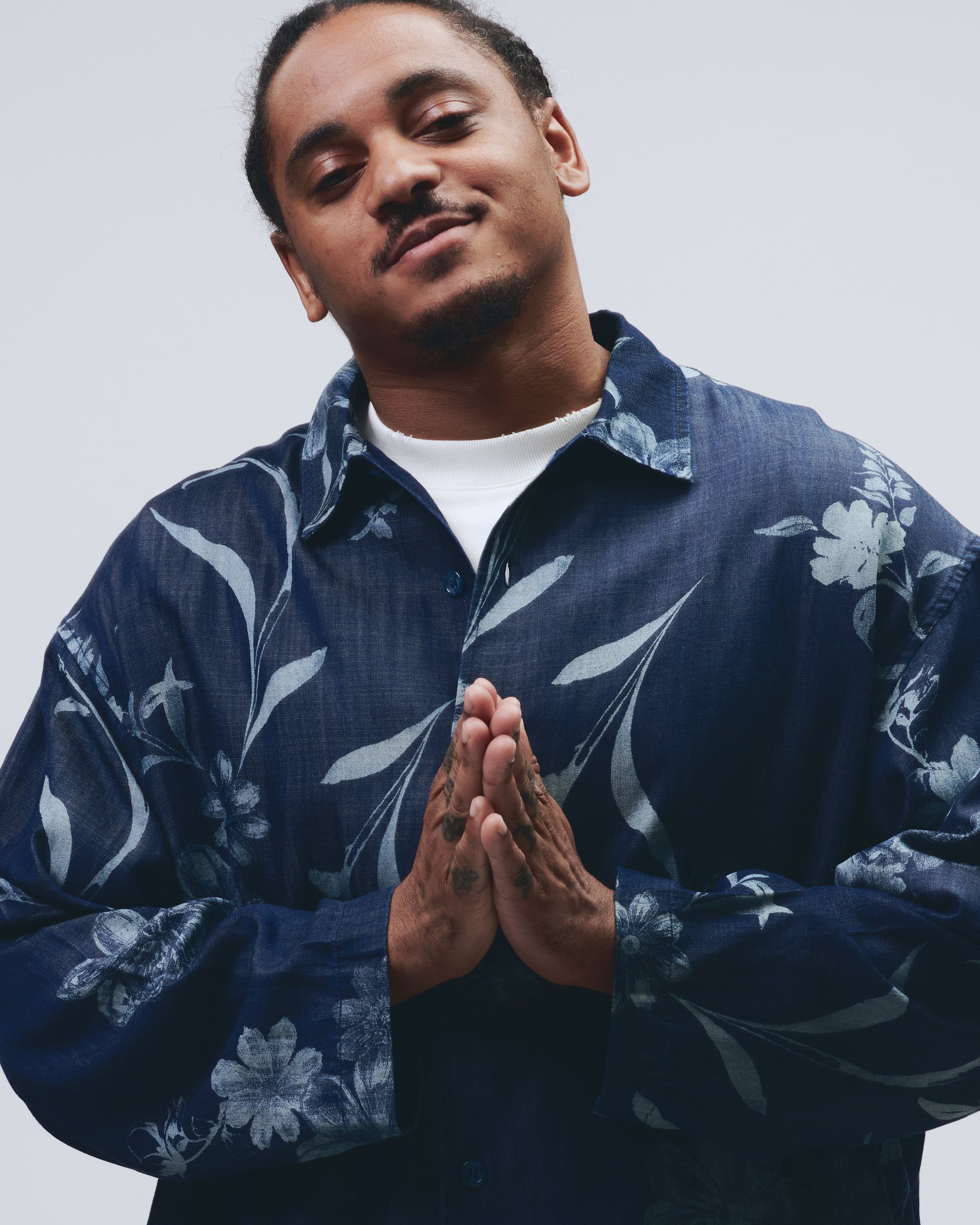 Kalvin Love wearing a navy floral shirt with hands pressed together against a light gray background